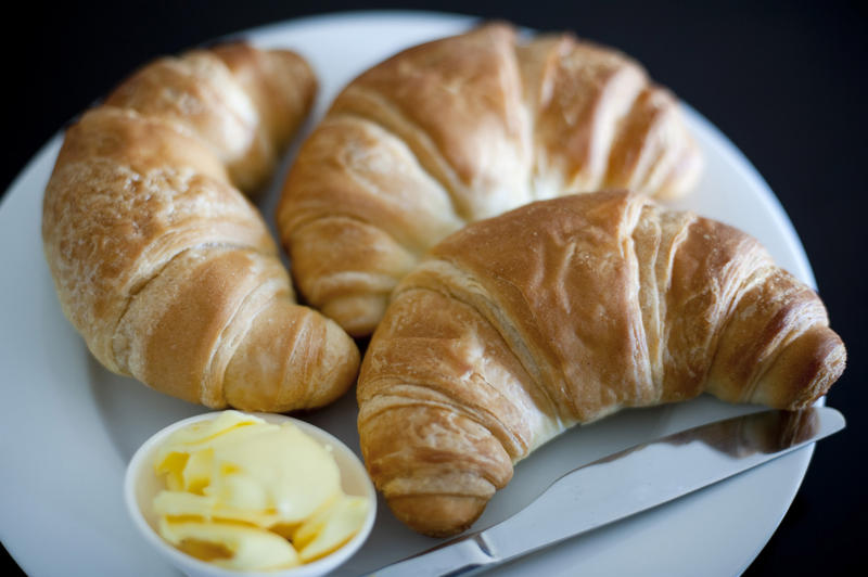 Three golden crescent shaped croissants made of rich flaky puff pastry served with butter for breakfast