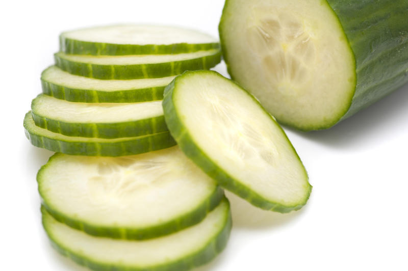 Close-up of a fresh nutritious cucumber with cut slices, on white background