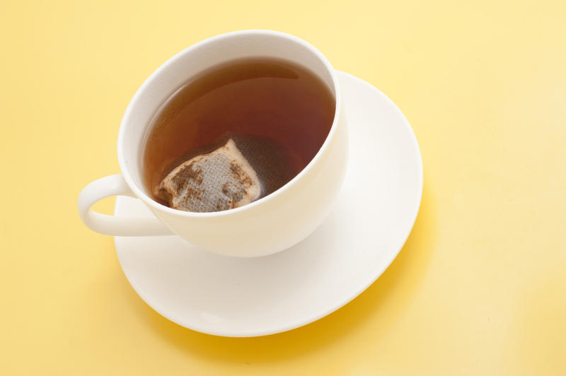 High angle view of a freshly brewed cup of black tea with a teabag inside steeping to the right strength on a yellow background with copyspace