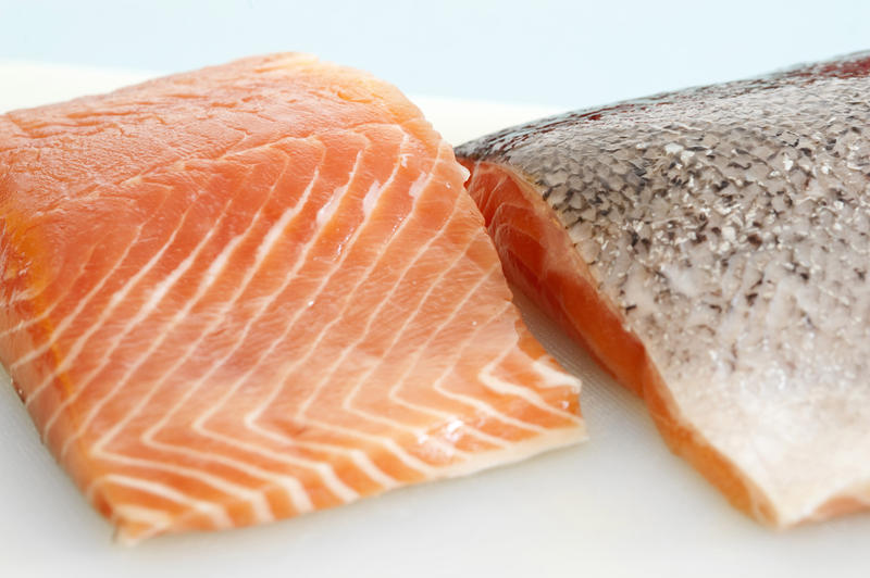 Close up view of two fresh uncooked salmon steaks on a plate, one facing down to reveal the skin
