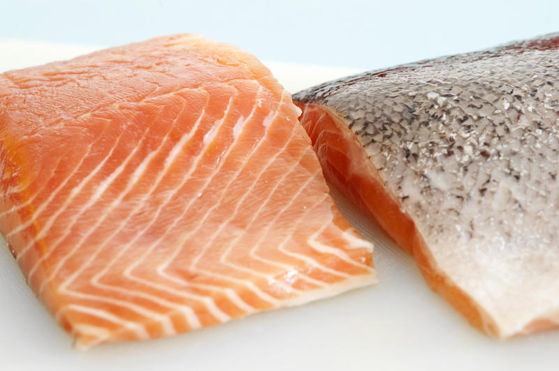 Close up view of two fresh uncooked salmon steaks on a plate, one facing down to reveal the skin