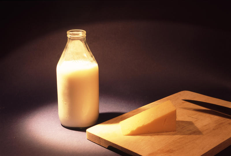 Glass bottle full of fresh creamy cows milk and a wedge of cheddar cheese on a cheeseboard over a dark background with copyspace