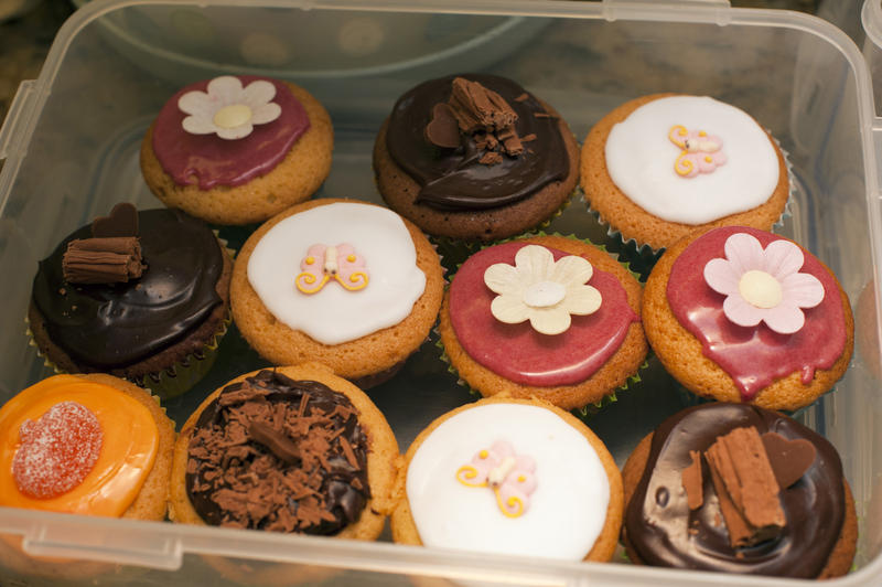 Plastic container filled with colorful decorated fairy cakes with assorted icing and flowers for a party or tea break