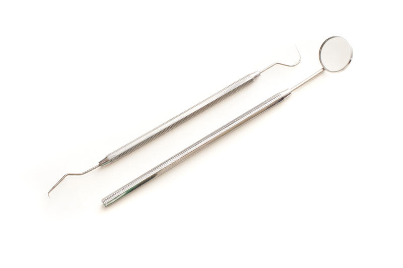 Dentists tools displayed on white with a stainless steel mirror and pick for examining teeth for caries and decay in his surgery, medical and healthcare concept