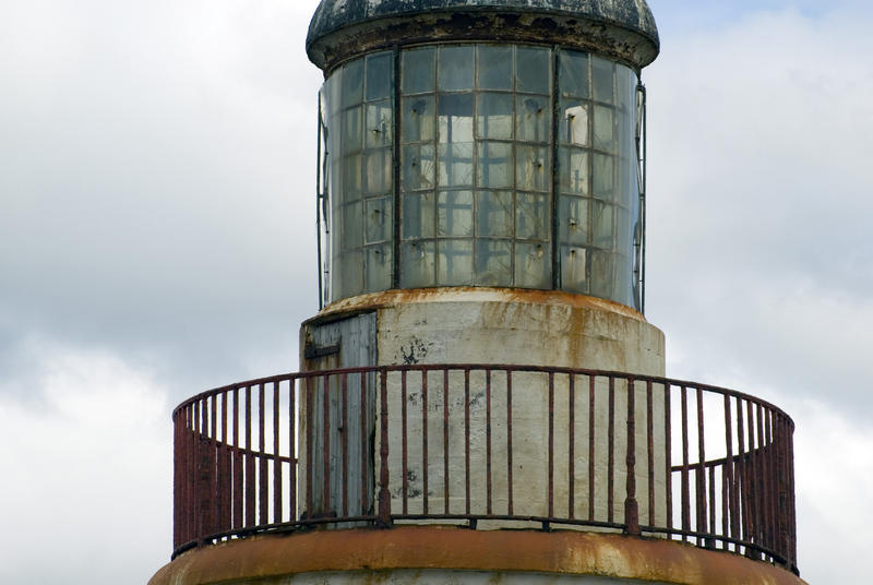 Closeup view of the lantern or lamp room of an old lighthouse against a cloudy sky