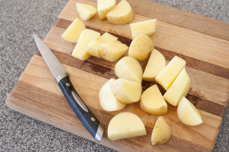 Close up Fresh Slices of Uncooked Healthy Potatoes on Wooden Cutting Board with Knife on the Side.