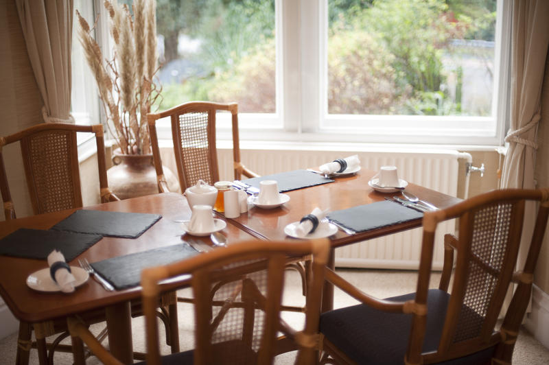 Hardwood dining table set for three people with stylish wicker back chairs in front of a bright window