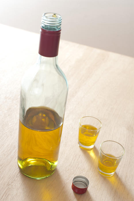 Opened unlabelled clear glass bottle of distilled whiskey with two full glasses alongside standing on a wooden counter, high angle view
