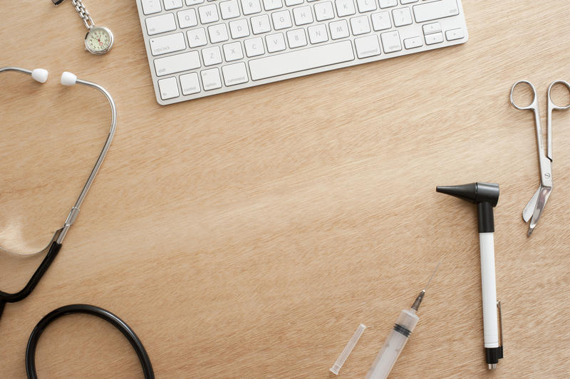 Medical or doctor backdrop with a high angle view of a laptop computer on a wooden desk with a border of medical equipment and central copyspace