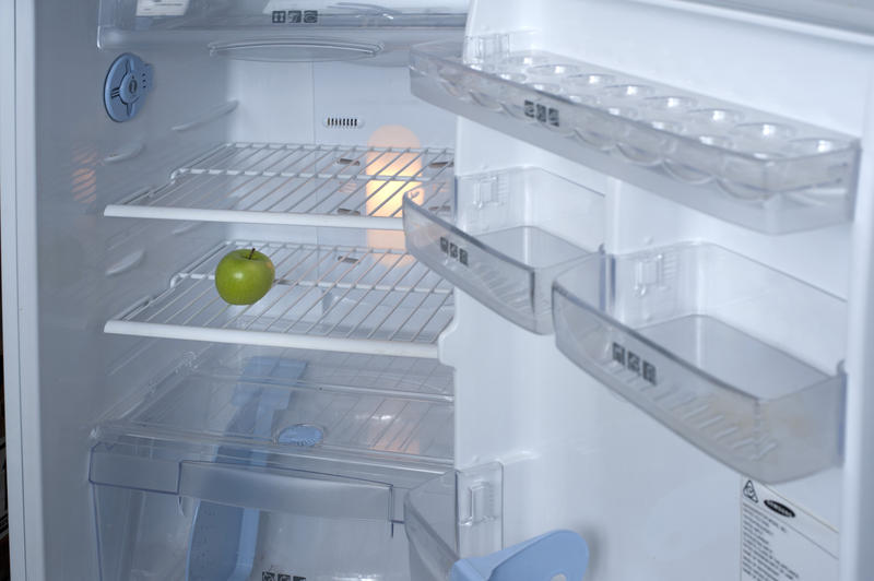 Interior of a small domestic refrigerator with the door open displaying the wire shelves and plastic storage containers and a single green apple