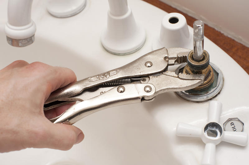 Man repairing a broken faucet or tap on a bathroom sink using a mole grip pliers in a DIY and renovation concept