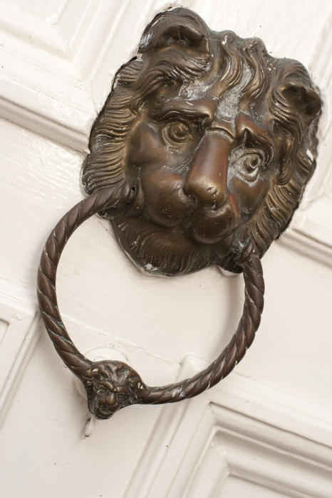 Bronze door knocker in the shape of a lions head with a ring in its mouth mounted on a wooden door