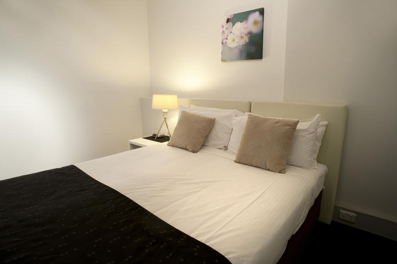 Double bed in a minimalist bedroom with neutral decor illuminated by a bedside lamp, close up view