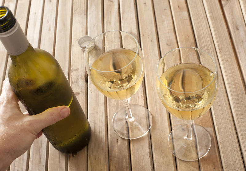 Man's hand holding bottle of white wine and two wine glasses standing on wooden table.