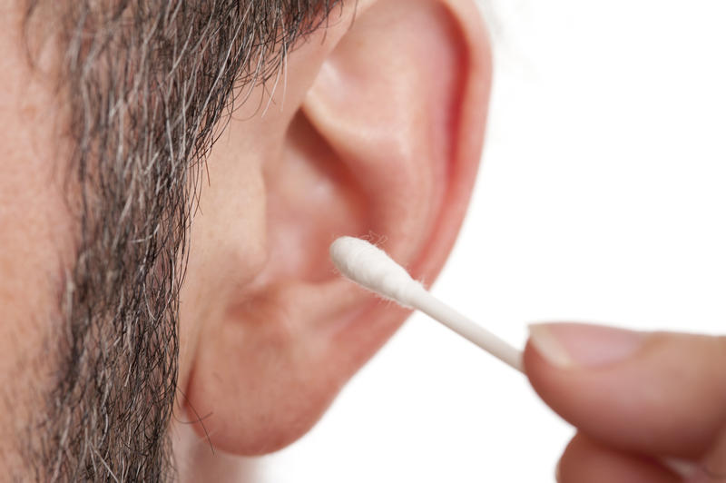 Man cleaning his ear with a cotton ear bud to remove the wax, close up view in a healthcare and hygiene concept