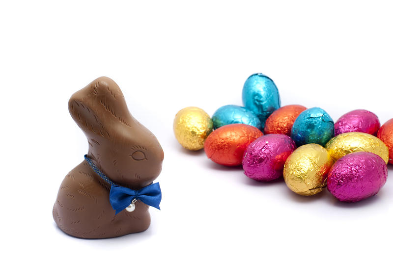 Chocolate Easter egg assortment with a cute little bunny with a bowtie in the foreground with numerous colourful foil wrapped eggs behind