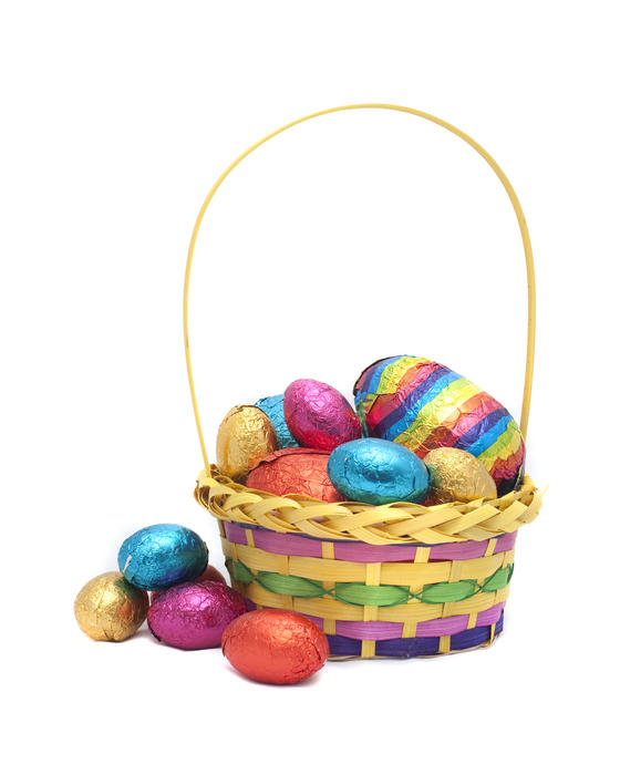 A decorative basket filled to overflowing with colourful foil wrapped Easter Eggs on a white background