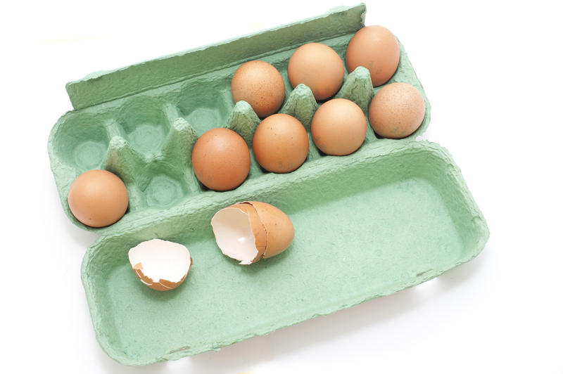 Fresh Brown Eggs on a Green Tray with Cracked Open Egg Shells Isolated on White Background