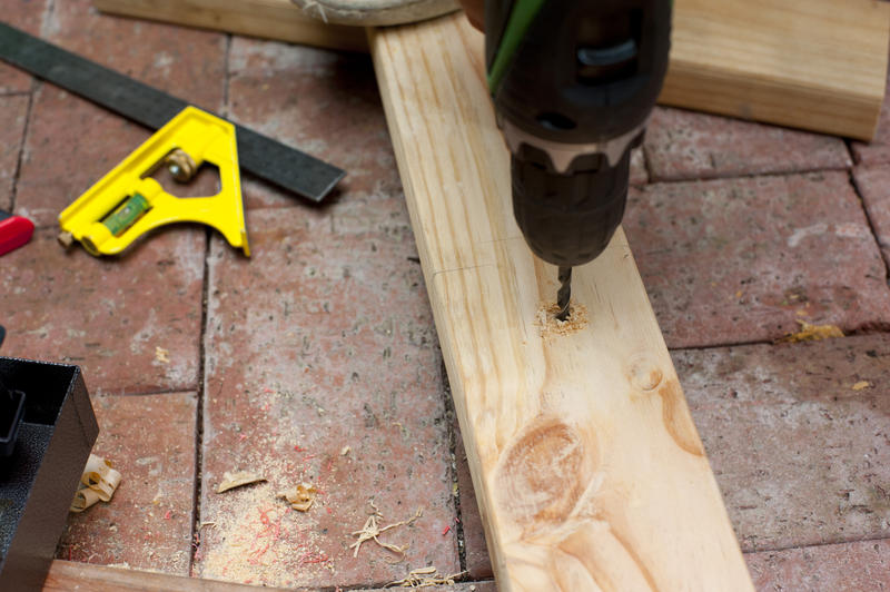 Drilling a hole in a plank of wood with a portable electric drill, close up view of the drill bit and wood