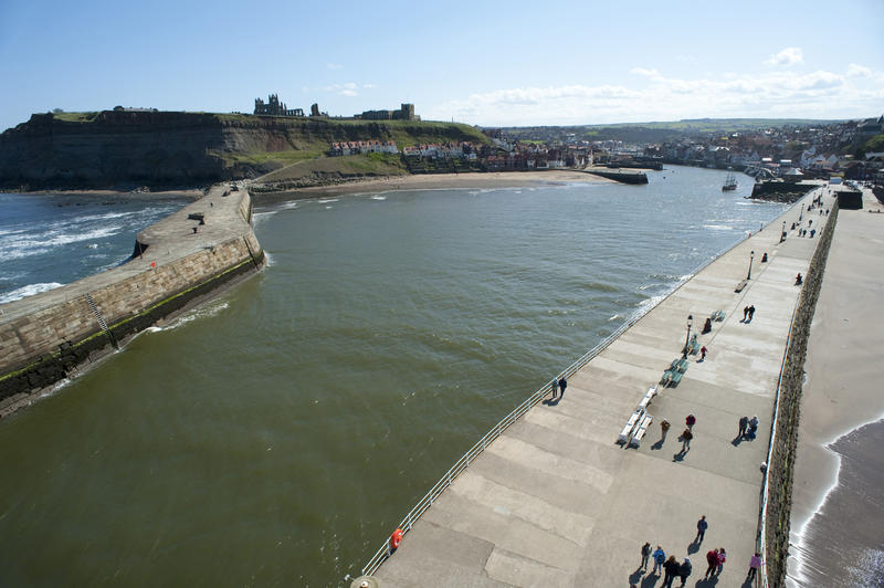 Aerial view of the Whitby piers looking back towards the town with people enjoying a walk along the promenade on top in the sunshine