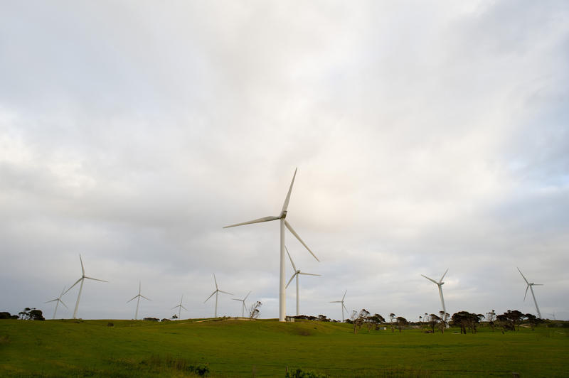 Wind turbines at a wind farm generating renewable electricity from the conversion of the kinetic energy of the wind, rural landscape against a cloudy sky