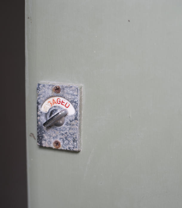 Closed white wooden door with a rotary lock showing an engaged sign to show that the interior room, washroom or public facility is occupied and in use