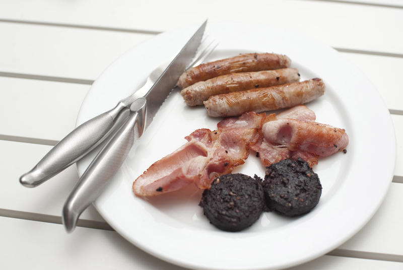 Fried breakfast with black pudding, rashers of crispy bacon and sausages served on a plain white plate