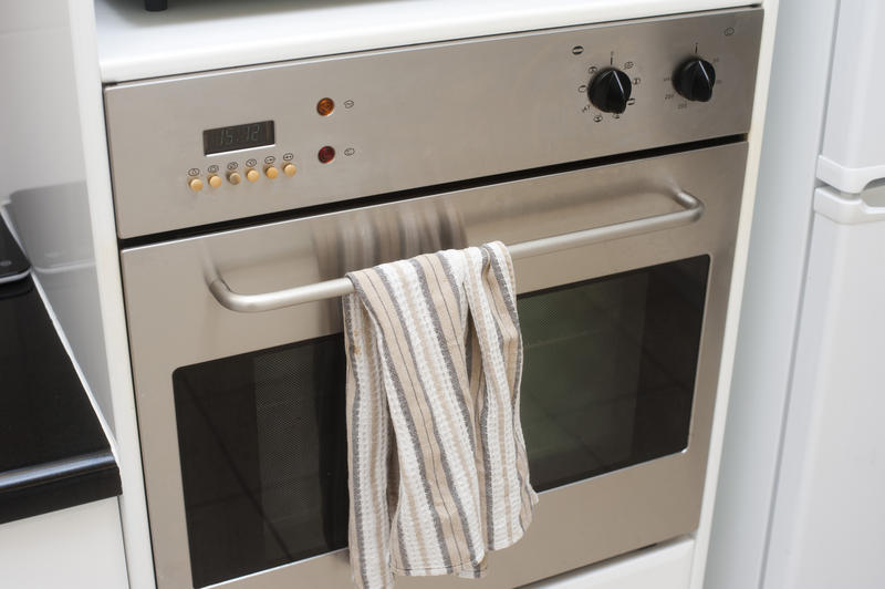 Modern metal domestic stove unit with a glass door and a dishcloth hanging from the handle