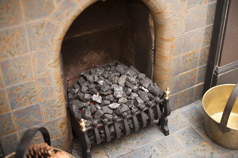 Close up of a tiled hearth with coal in the grate and antique brass cauldrons with wood and cones on either side, interior decor concept
