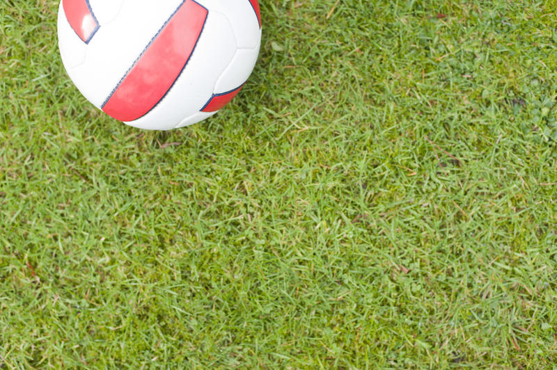 Football or soccer ball on neat manicured green grass with the red English colors on white, high angle view with plenty of copyspace