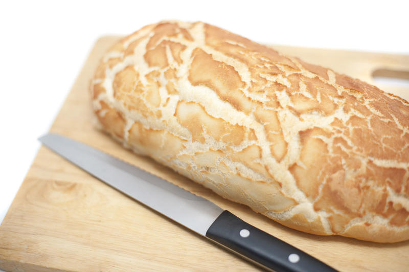Whole uncut loaf of freshly baked crisp crusty bread on a wooden bread board with a knife over a white background