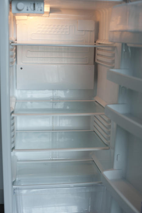 Open empty white refrigerator interior with shelves and compartments illuminated by the interior light showing it is on and connected to electricity