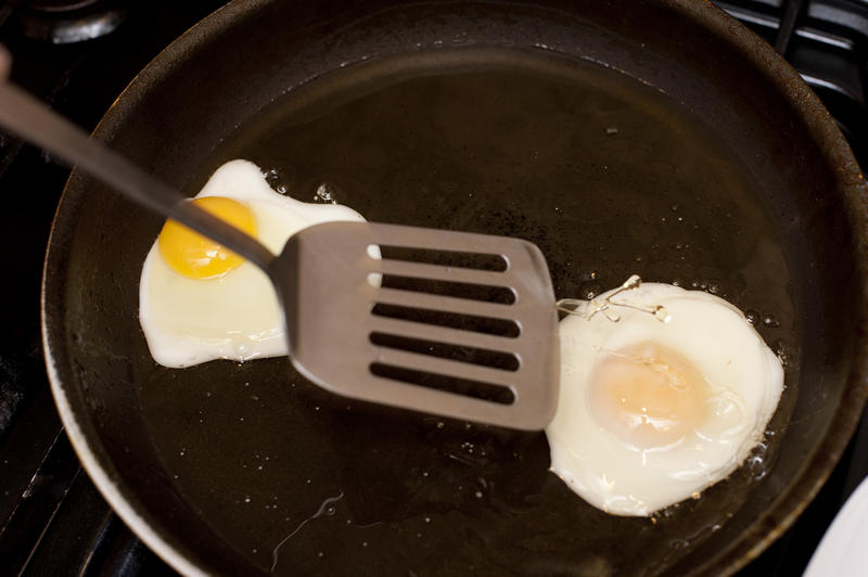 Fried eggs in a non-stick frying pan with a metal kitchen lifter ready to serve them for breakfast