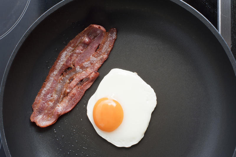 Overhead view of a fried egg and rasher of crisp bacon for breakfast in a non-stick frying pan