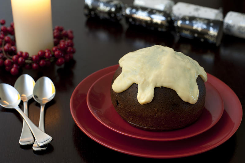 Traditional steamed Christmas plum pudding with its rich fruity texture topped with brandy custard and served on a festive table with a glowing candle