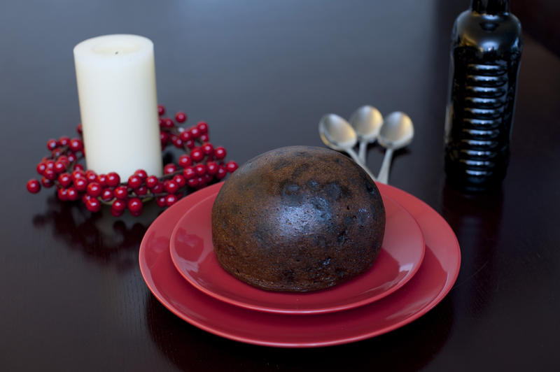Traditional steamed Christmas fruit pudding on a festive table with a candle and colourful wreath of red berries