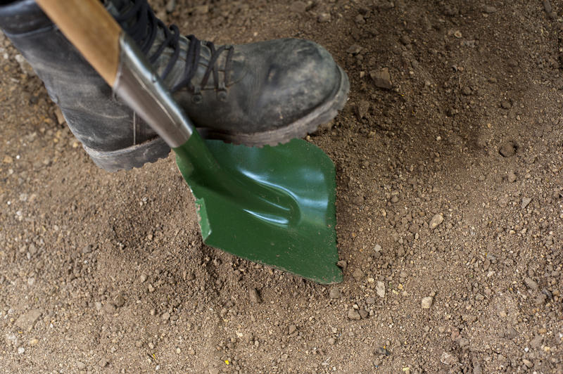 High angle view of a green garden spade standing on the ground alongside old sturdy boots for working in the garden