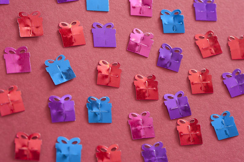 Gift background of decorative colorful gifts shapes scattered randomly on a red background in a full frame overhead view for a celebration or special occasion