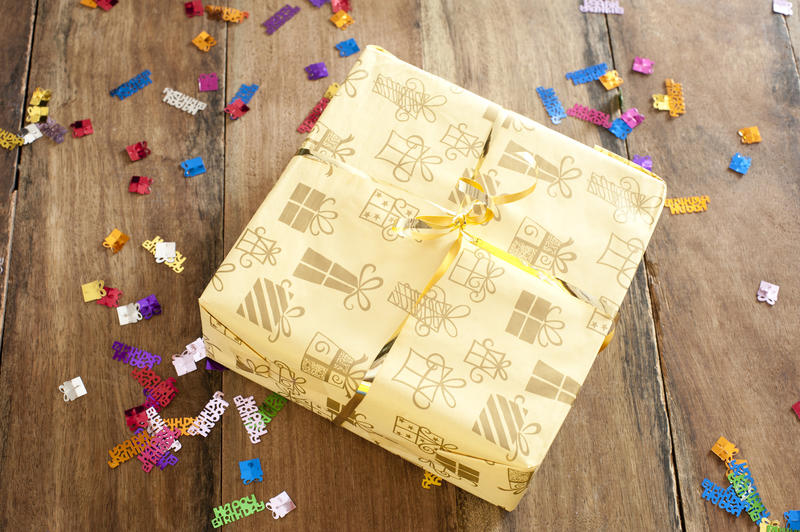 High Angle View of Yellow Birthday Gift Box on Top of a Wooden Table with Colored Confetti Scattered Around