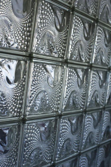 Oblique view of a wall composed of translucent glass bricks with a textured undulating wavy pattern of small dots