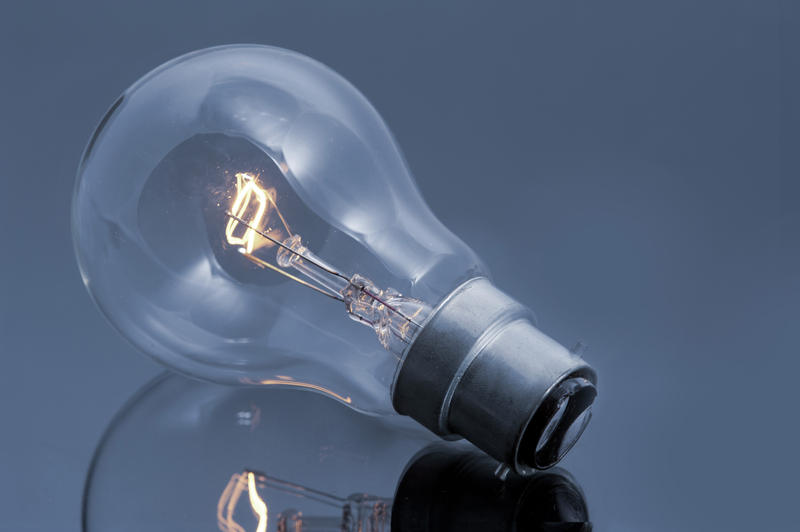 Close up Conceptual Glowing Light Bulb on Top of Glossy Gray Table, Emphasizing Reflection.