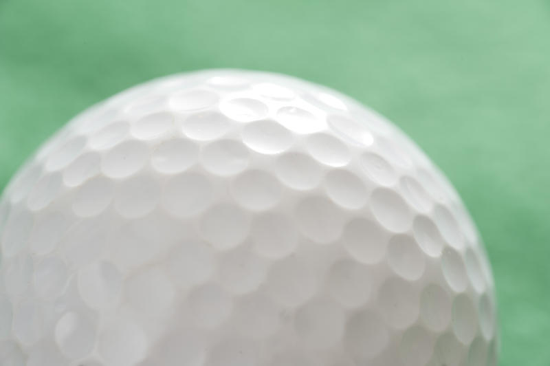 Close up of a white golf ball showing the traditional dimpled texture over a green background
