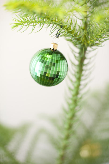 Green Christmas bauble hanging on a natural pine tree decorated to celebrate the Xmas season, close up with copyspace