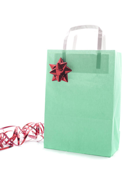 Green Christmas gift bag decorated with an ornamental metallic foil bow and coiled ribbon, close up isolated on white with copyspace