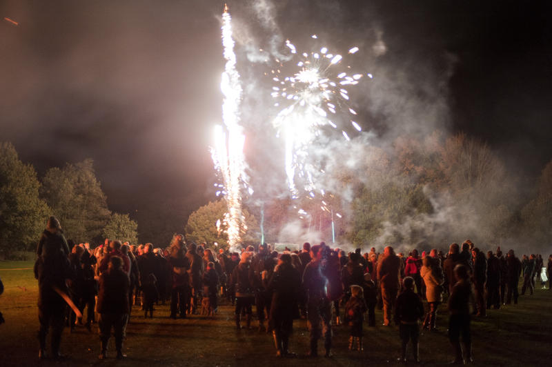 Crowd of people watching a fireworks display in an outdoor field as colorful exploding rockets light up the night sky during a Bonfire Night or Guy Fawkes celebration