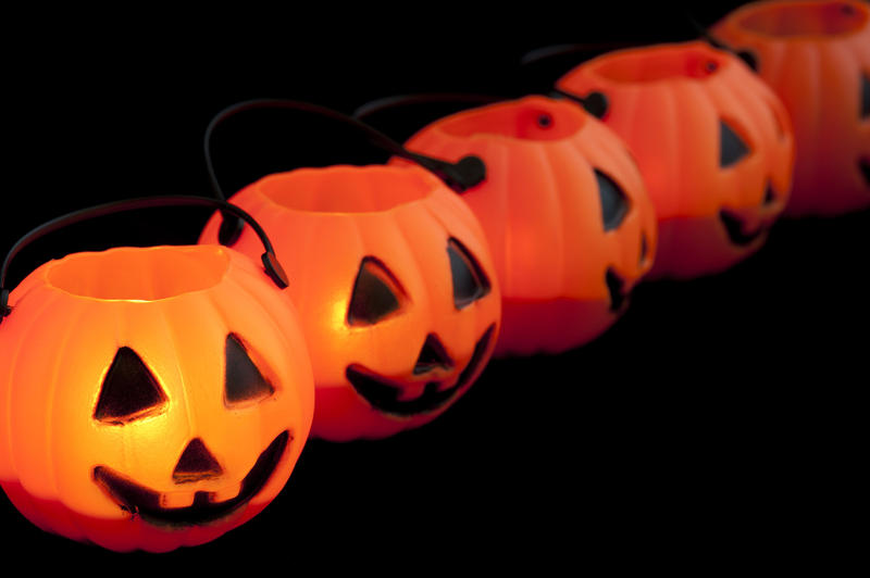 Diagonal row of fun ornamental orange Halloween jack-o-lanterns in the shape of pumpkins with freaky faces on a black background