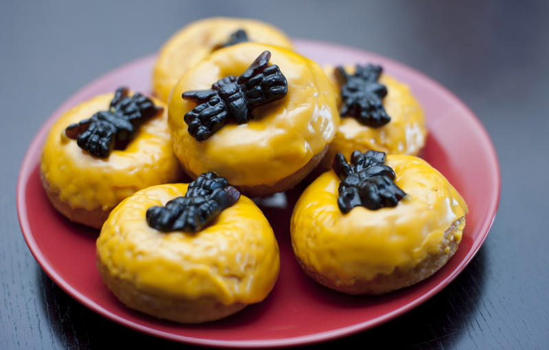 Orange halloween party doughnut snacks topped with creepy black jelly spiders served on a plate for a fun treat during trick-or-treating