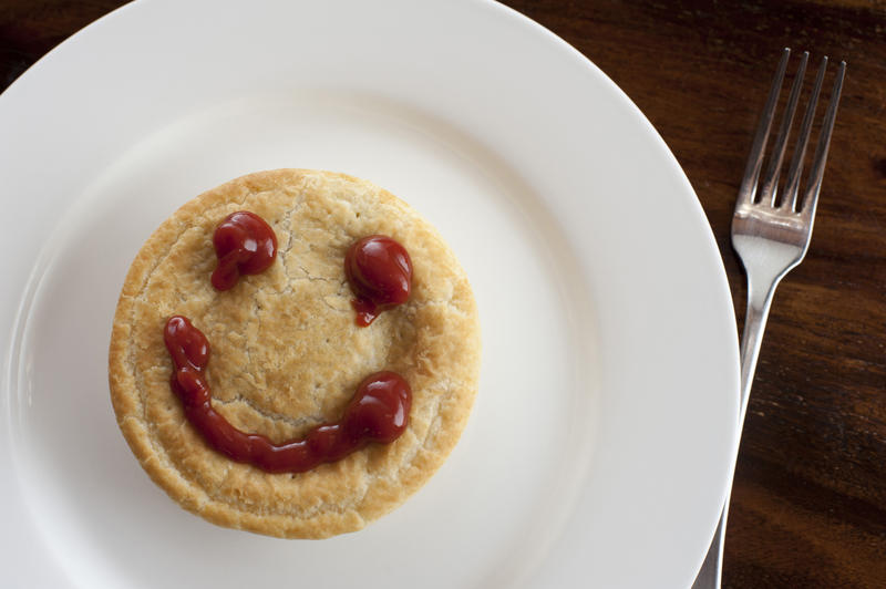 Happy meat pie with a smiley face formed of rich brown gravy on top of the pastry crust, overhead view on a plate