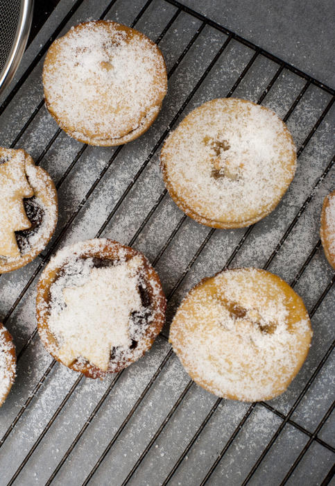 Traditional home baked fruity Christmas mince pies with golden crisp pastry crusts sprinkled with icing sugar on a rack in the kitchen, overhead view