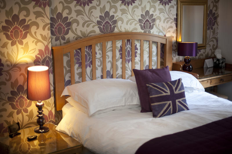 Patriotic British bed with Union Jack cushions in a homely bedroom with floral wallpaper